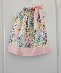 a dress hanging on a door with a pink bow at the top and flowers all over it