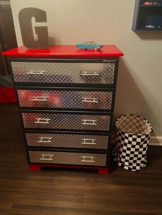 a red and black dresser sitting next to a toy car on top of a wooden floor