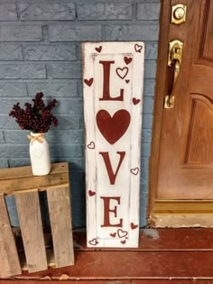 a wooden sign that says love with hearts on it next to a planter and door