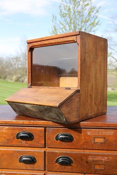 an old fashioned wooden box sitting on top of a dresser in front of a green field