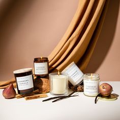 an assortment of candles, apples and cinnamons on a white table with a brown curtain in the background