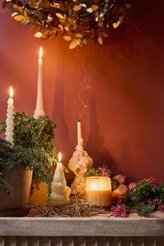 candles are lit on a mantle with greenery