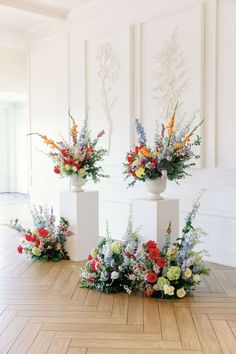 three white vases filled with colorful flowers sitting on top of a hard wood floor