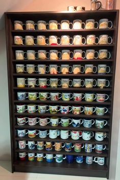 a shelf filled with lots of coffee mugs on top of each other in front of a wall