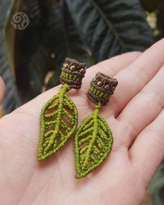 a pair of green leaf shaped earrings sitting on top of a hand