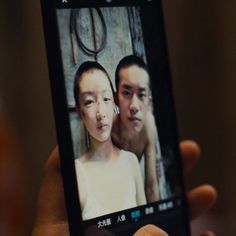 a person holding up a cell phone with an image of two people on the screen