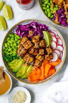 two bowls filled with different types of food on top of a white table next to dipping sauce