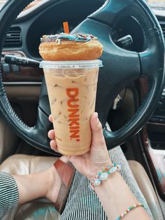 a person holding up a drink in front of a steering wheel with doughnuts on it