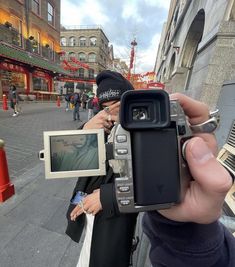 a person holding up a camera in front of a building on a city street with people walking around