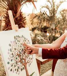 the bride and groom are holding their hands near an easel with a tree on it