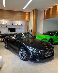 two cars are parked in a showroom, one is black and the other is green