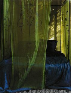 a bed with green curtains hanging over it's headboard and pillows on the floor