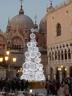 a lit christmas tree in the middle of a plaza with many people walking around it