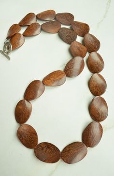 One long strand of dark brown wood beads with brown glass spacer beads. The wood color may vary from what you see on the screen due to the nature of wood. - Length is 38" (can vary depending on the beads) - Beads measure 1.5" by 1"- Lead free pewter toggle (gold toggle and stainless steel clasp also available) The necklace length can be customized. The mannequin's neck size is 15". We do not recommend double wrapping this necklace. Matching earrings: https://www.danaleblanc.com/products/brown-wo Brown Wooden Beads Oval Jewelry, Brown Wooden Oval Beads Jewelry, Brown Jewelry With Oval Wooden Beads, Artisan Brown Beaded Necklaces With Oval Beads, Artisan Brown Beaded Necklace With Oval Beads, Brown Wooden Beaded Jewelry, Mahogany Wooden Beads Jewelry, Mahogany Colored Wooden Bead Jewelry, Brown Wood Bead Jewelry