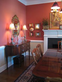 a dining room with red walls and wooden table surrounded by chairs in front of a fireplace