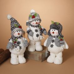 three knitted snowmen standing next to each other on a wooden block with a brown background