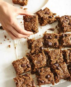 chocolate chip cookie bars on a white plate with a hand reaching for one piece from the tray