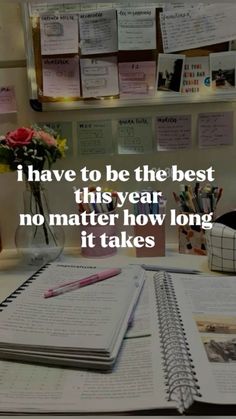 an open notebook sitting on top of a desk next to a vase filled with flowers