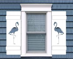 two flamingos are standing in the window sill next to a blue house with white trim