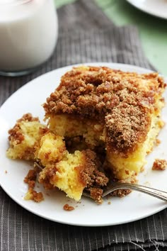 a white plate topped with a piece of cake next to a glass of milk and a fork