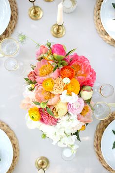 an arrangement of colorful flowers on a table with gold plates and candles in the background