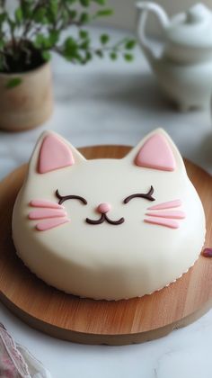 a white cat cake sitting on top of a wooden plate