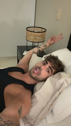 a man laying in bed with tattoos on his arm and chest, making the peace sign