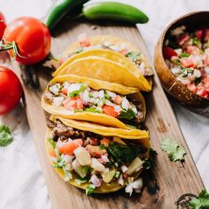 three tacos on a cutting board with tomatoes and peppers