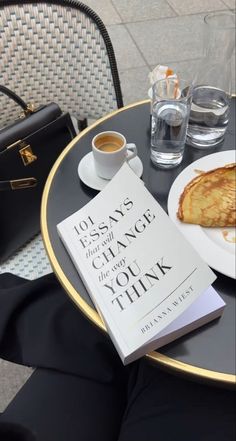 a table topped with a plate of food next to a cup of coffee and a book