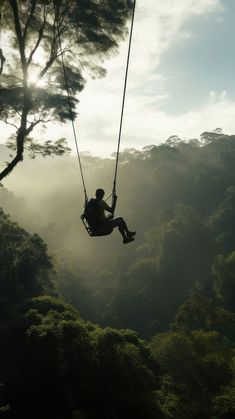 a man is swinging from a rope in the air above trees and mountains, while sun shines through the clouds