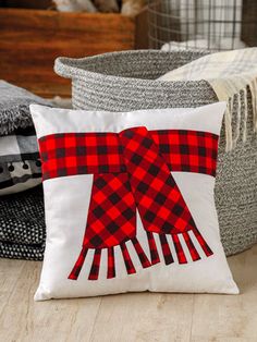 a red and black plaid bow pillow sitting on top of a wooden floor next to blankets