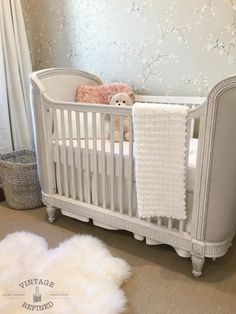 a white crib with a teddy bear in it and a rug on the floor