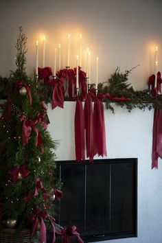 a fireplace decorated for christmas with candles and red bows on the mantel above it