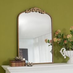 a mirror sitting on top of a mantle next to a vase with flowers in it