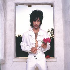 a man in white is holding a rose and posing for the camera with his shirt open