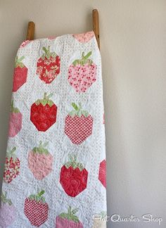 a white quilt with red and pink strawberries on it hanging from a clothes line