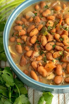 a blue bowl filled with beans next to cilantro and celery leaves