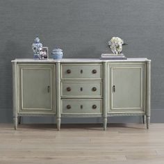 an antique sideboard with drawers and vases on top, against a gray wall