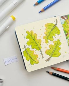 an open notebook with watercolors and pencils next to it