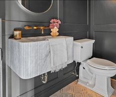 a white toilet sitting next to a sink in a bathroom under a mirror and a gold faucet