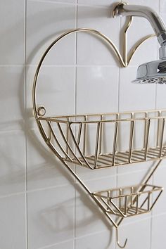 a heart shaped basket hanging on the wall next to a faucet and shower head