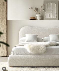 a white bed sitting in a bedroom next to a vase with flowers on top of it