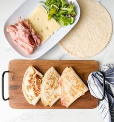 three quesadillas on a wooden cutting board with cheese and lettuce