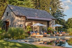 an outdoor pool with lounge chairs and umbrellas next to it, surrounded by trees