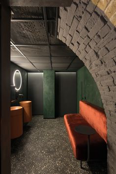 an orange bench sitting in the middle of a room next to a brick wall and round mirror