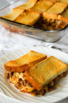 two plates with sandwiches on them next to a casserole dish filled with meat and cheese