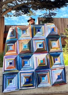 a man standing next to a large quilt on top of a cement slab in front of a tree