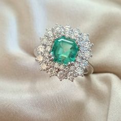 an emerald and diamond ring sitting on top of a white cloth