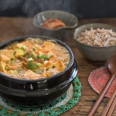 a bowl of soup with chopsticks and rice on a table next to it