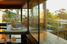 the inside of a house with glass walls and wood flooring, looking out onto an outdoor deck area